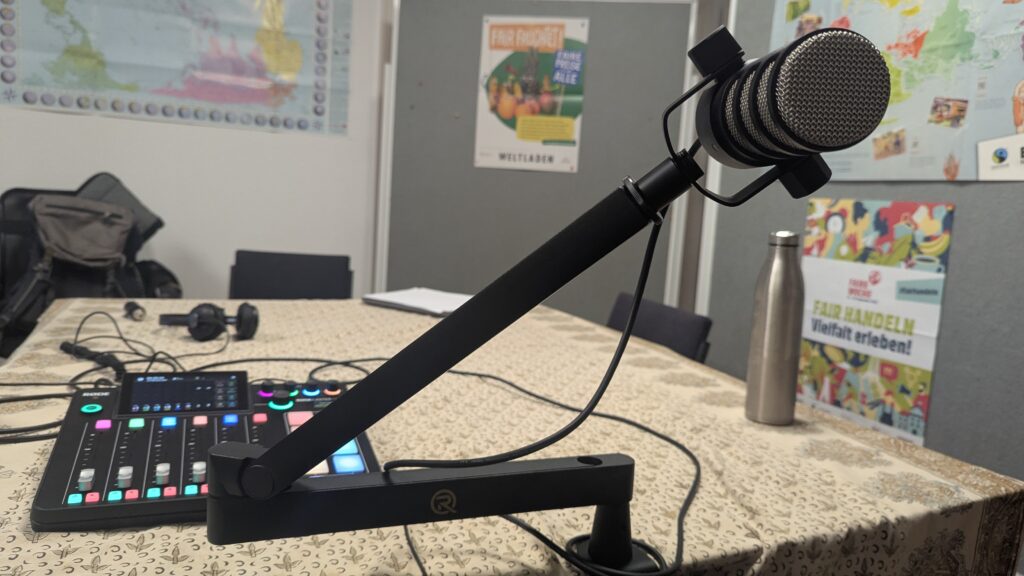 Ein Podcastmikrofon und ein Mischpult, dahinter sieht man Materialien aus dem globalen Lernen.